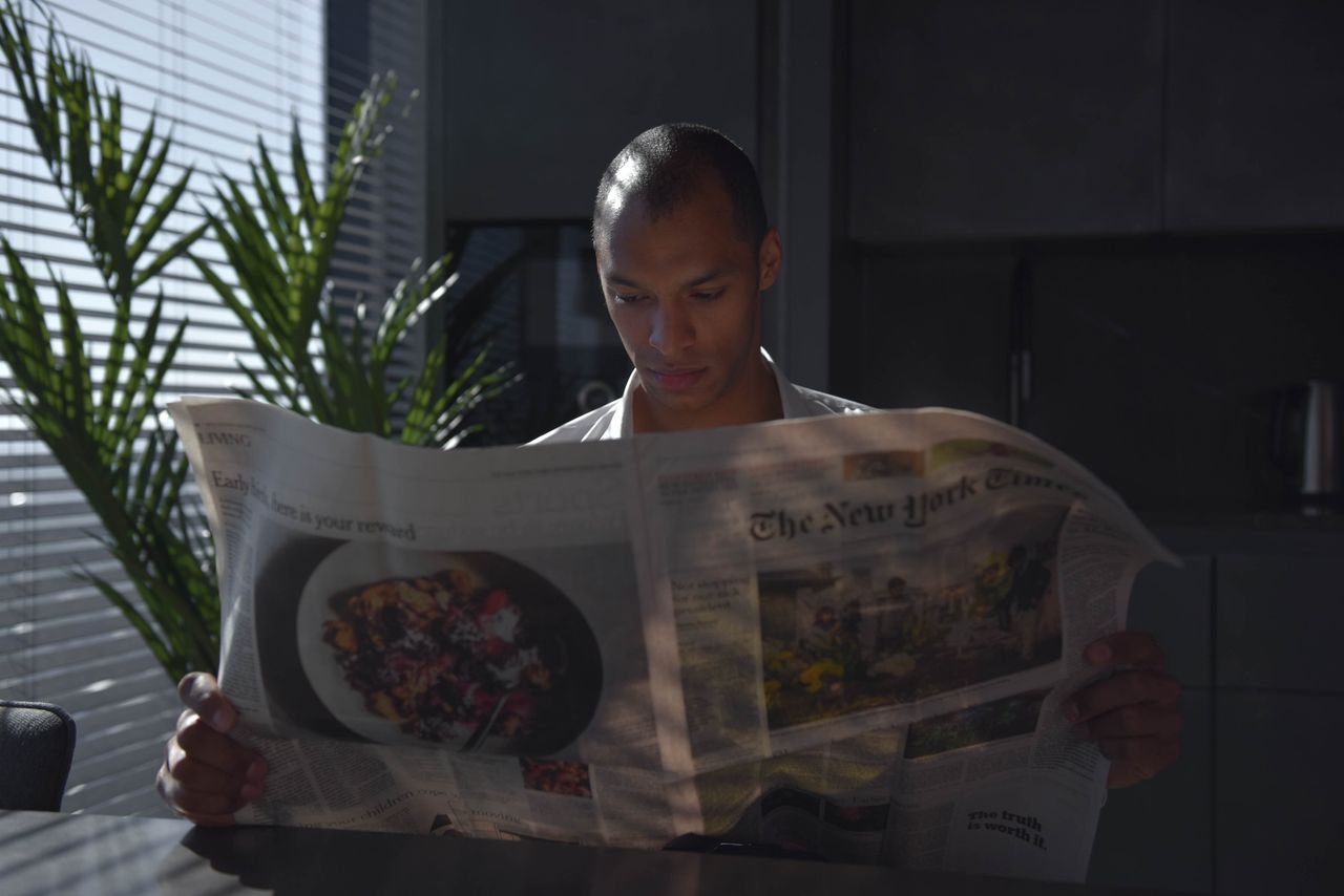 Businessman focused on reading newspaper in a sunny indoor office setting.